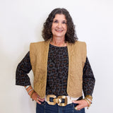 Woman wearing a leopard print top, beige vest, and blue jeans against a white background