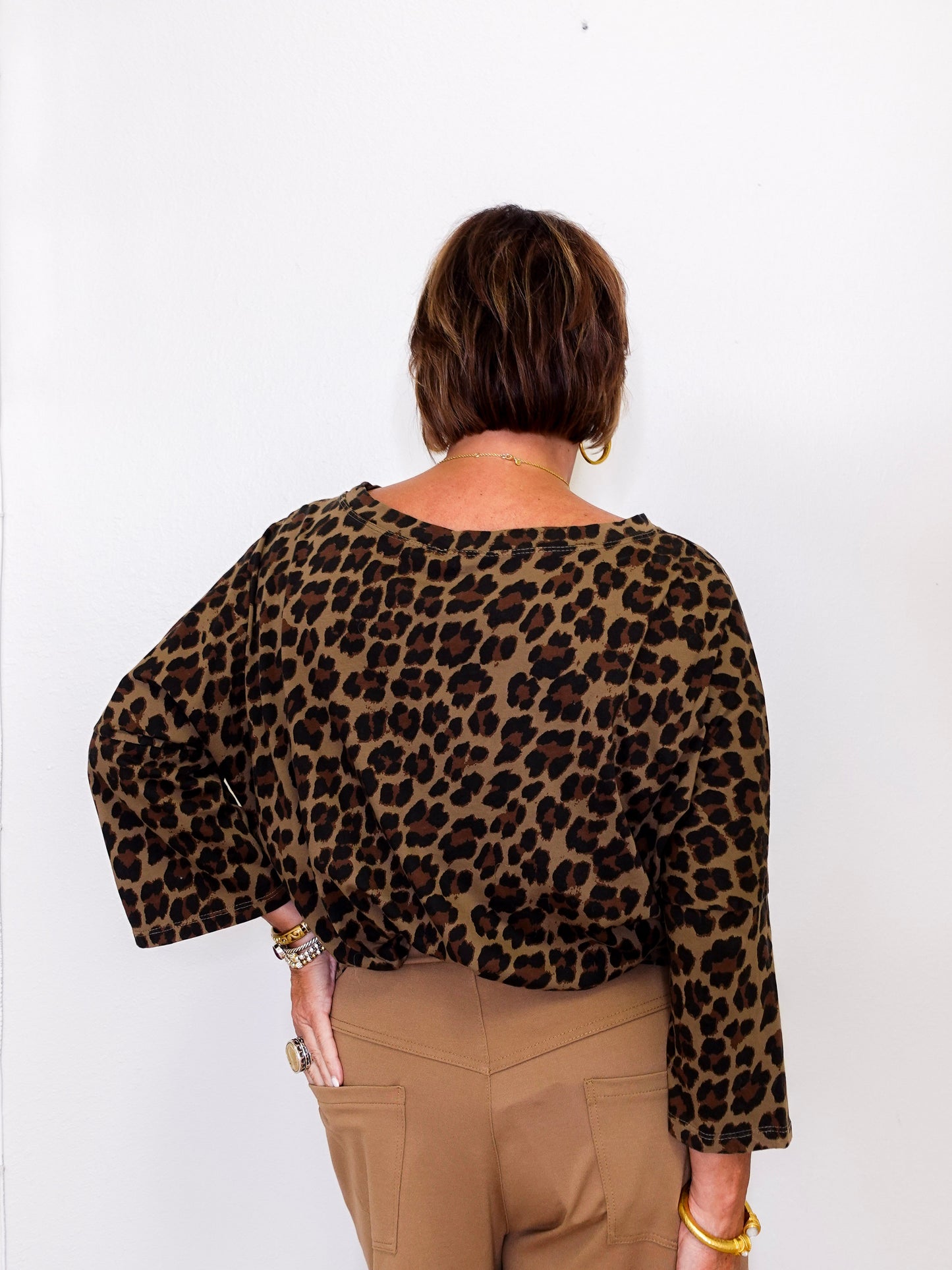 Person wearing a leopard print top and beige pants against a white background