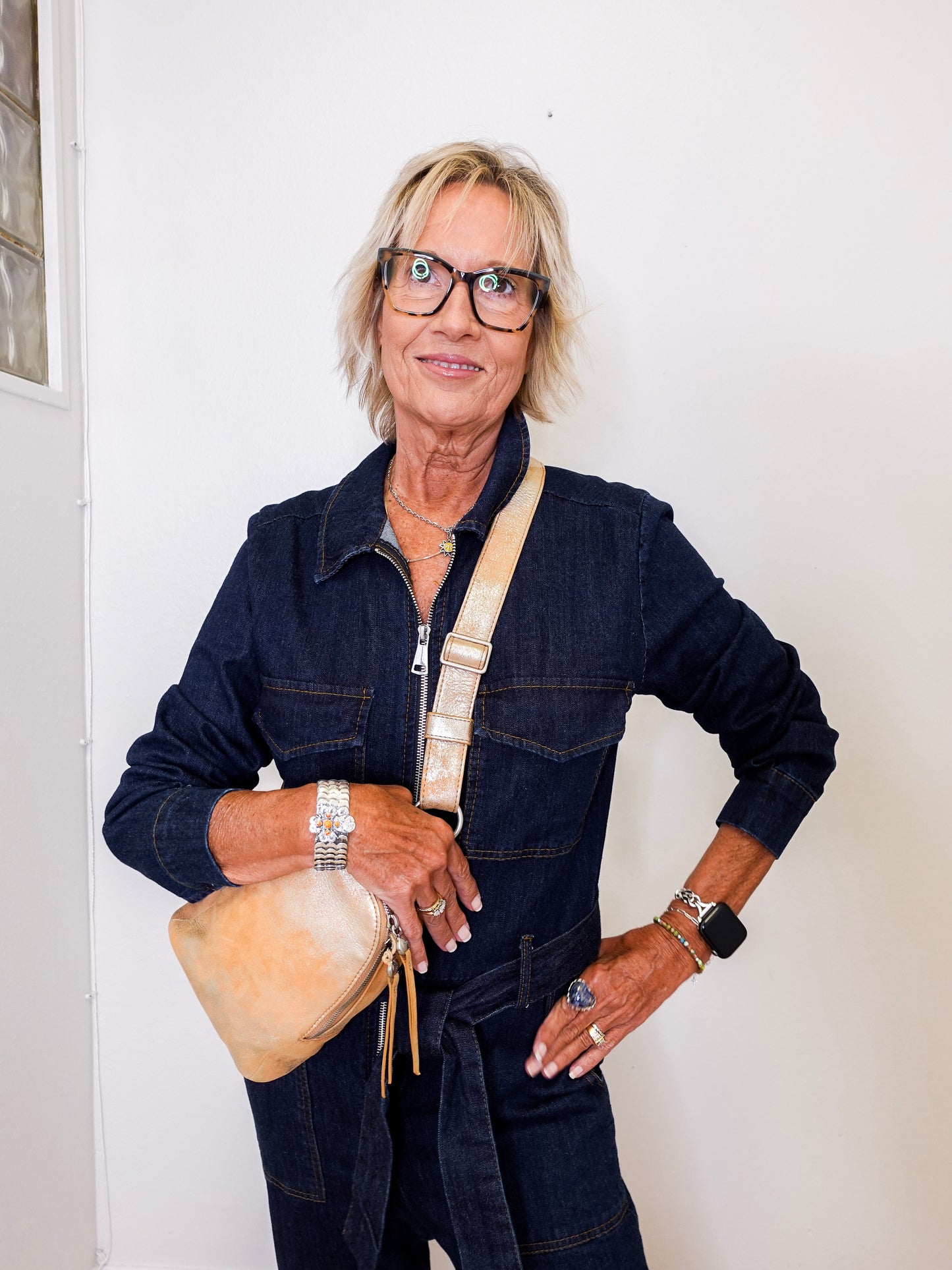Woman wearing a denim jumpsuit with a beige bag against a white wall