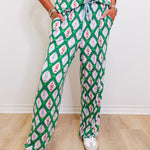 Person wearing a green and pink patterned outfit with white shoes on a light wooden floor.