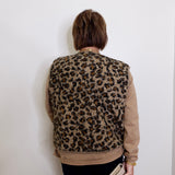 Person wearing a leopard print vest against a white wall