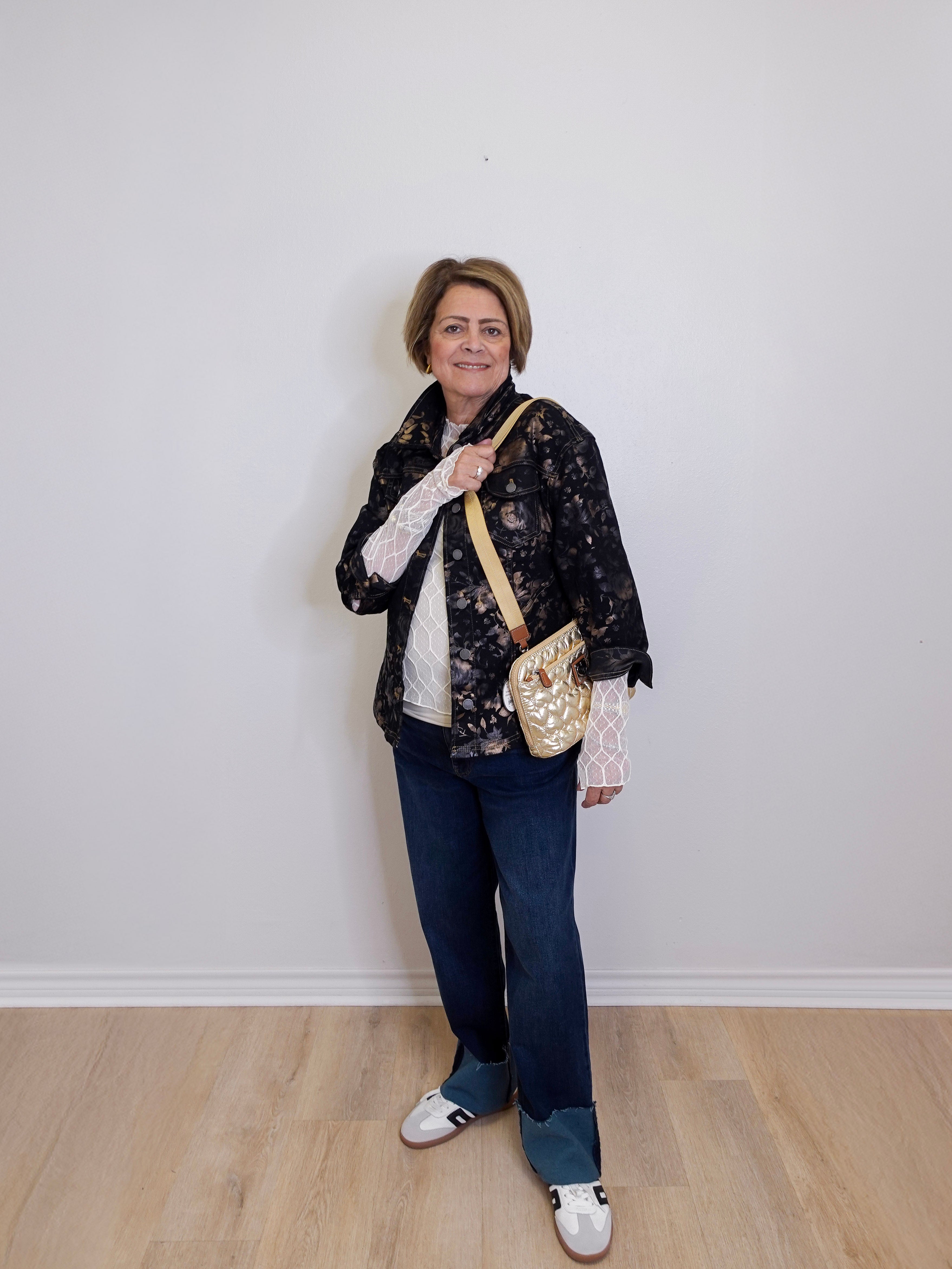 Woman standing against a white wall holding a gold handbag.