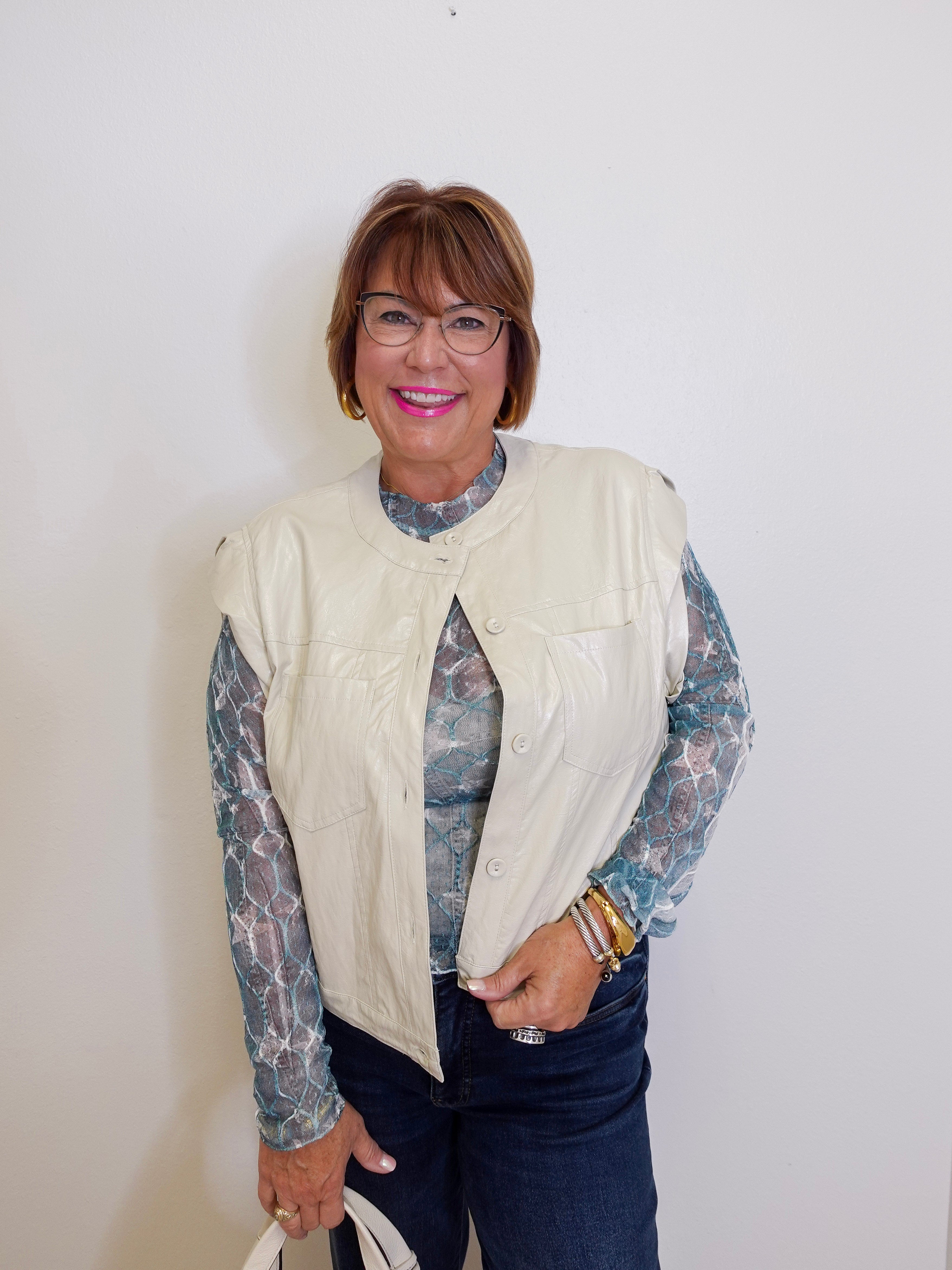 Woman wearing a cream vest over a patterned shirt with a plain background