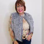 Woman wearing a gray fur vest over a patterned top against a white background