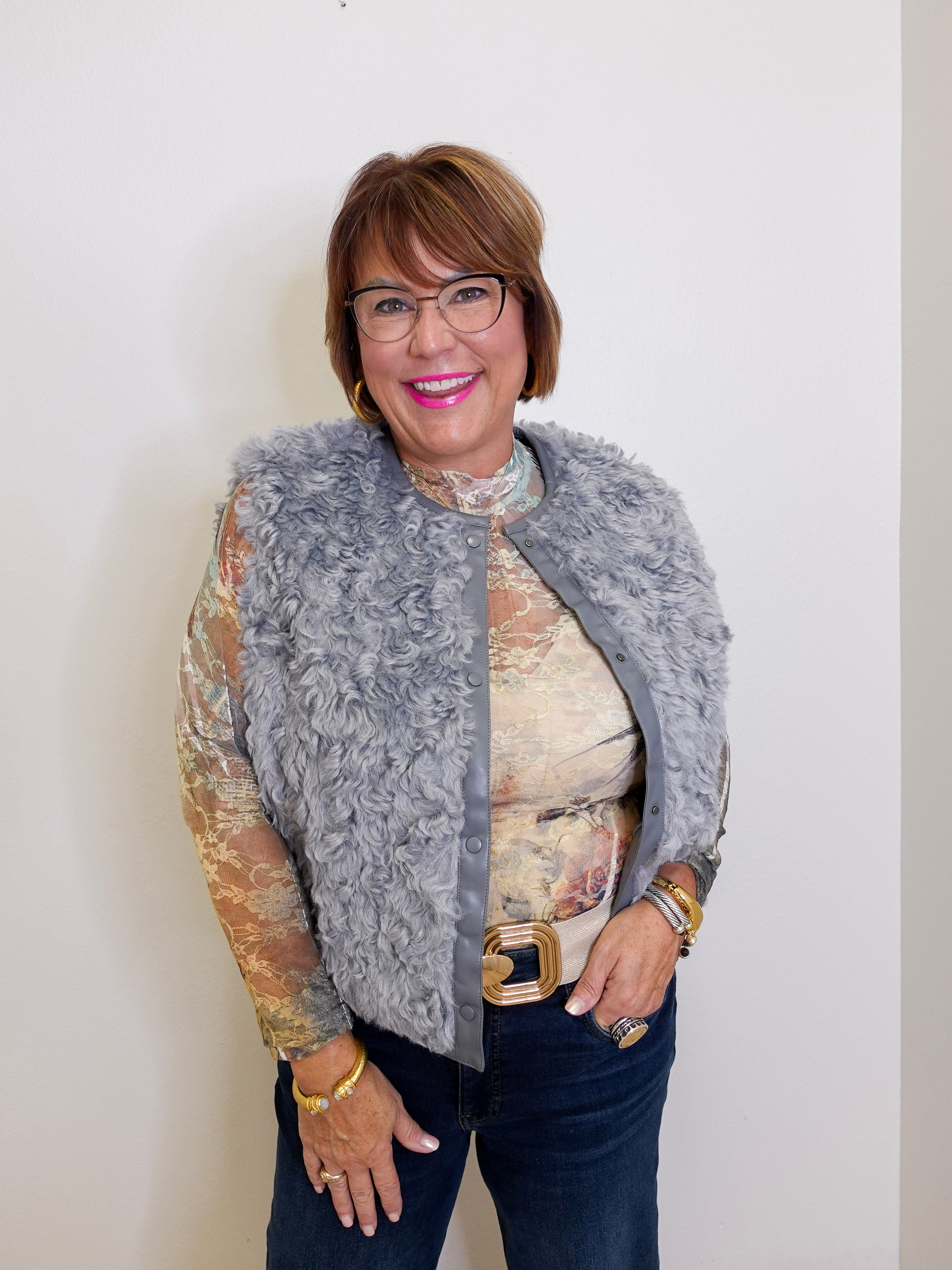 Woman wearing a gray fur vest over a patterned top against a white background