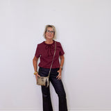 Woman wearing a burgundy top and black pants, standing against a white wall.