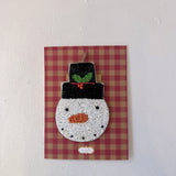 Decorative snowman ornament on a red and brown checkered background