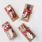 Four Christmas-themed metal spoons on packaging with Santa and reindeer designs on a white background.