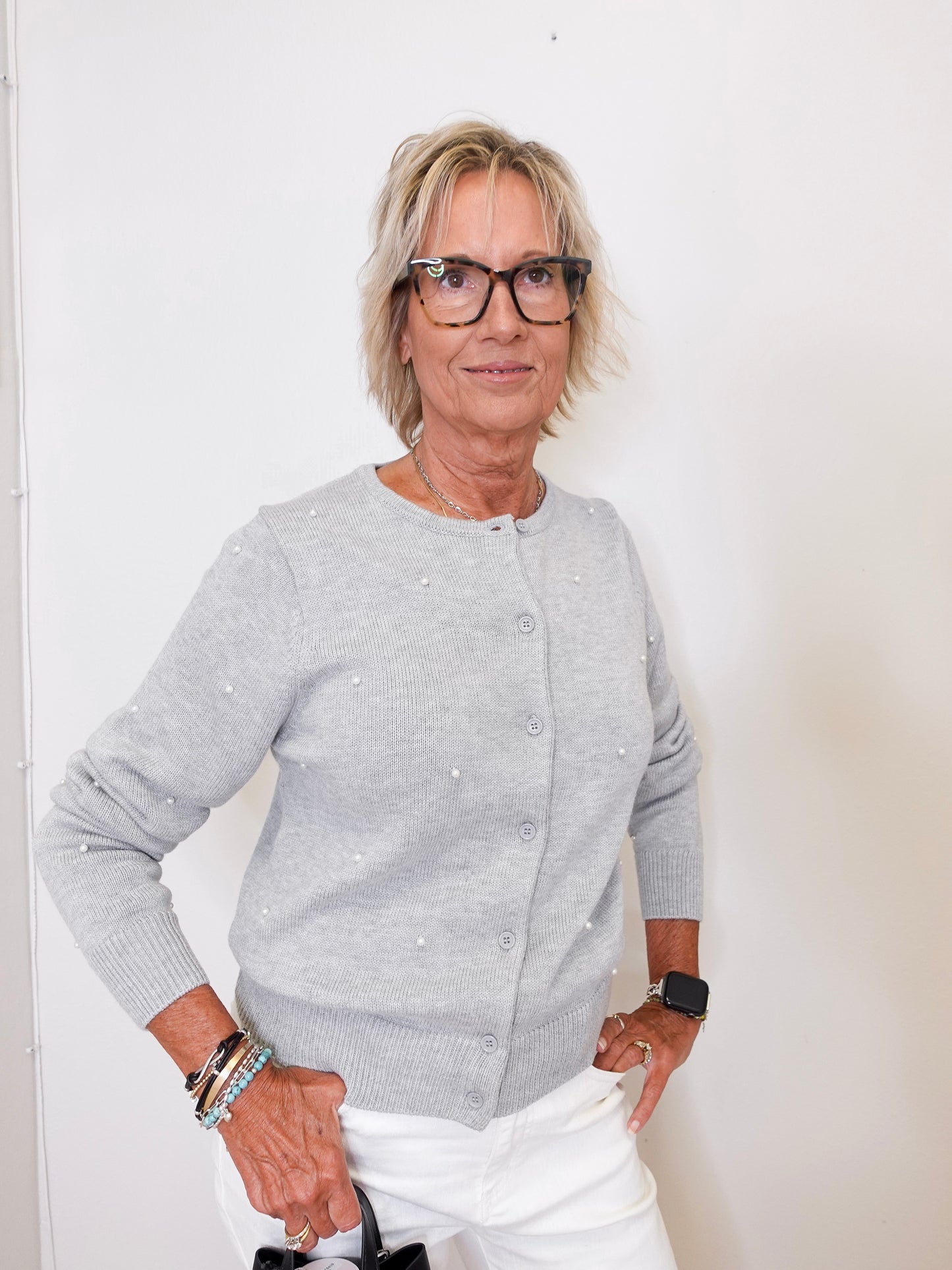 Woman wearing a gray cardigan and white pants against a plain background