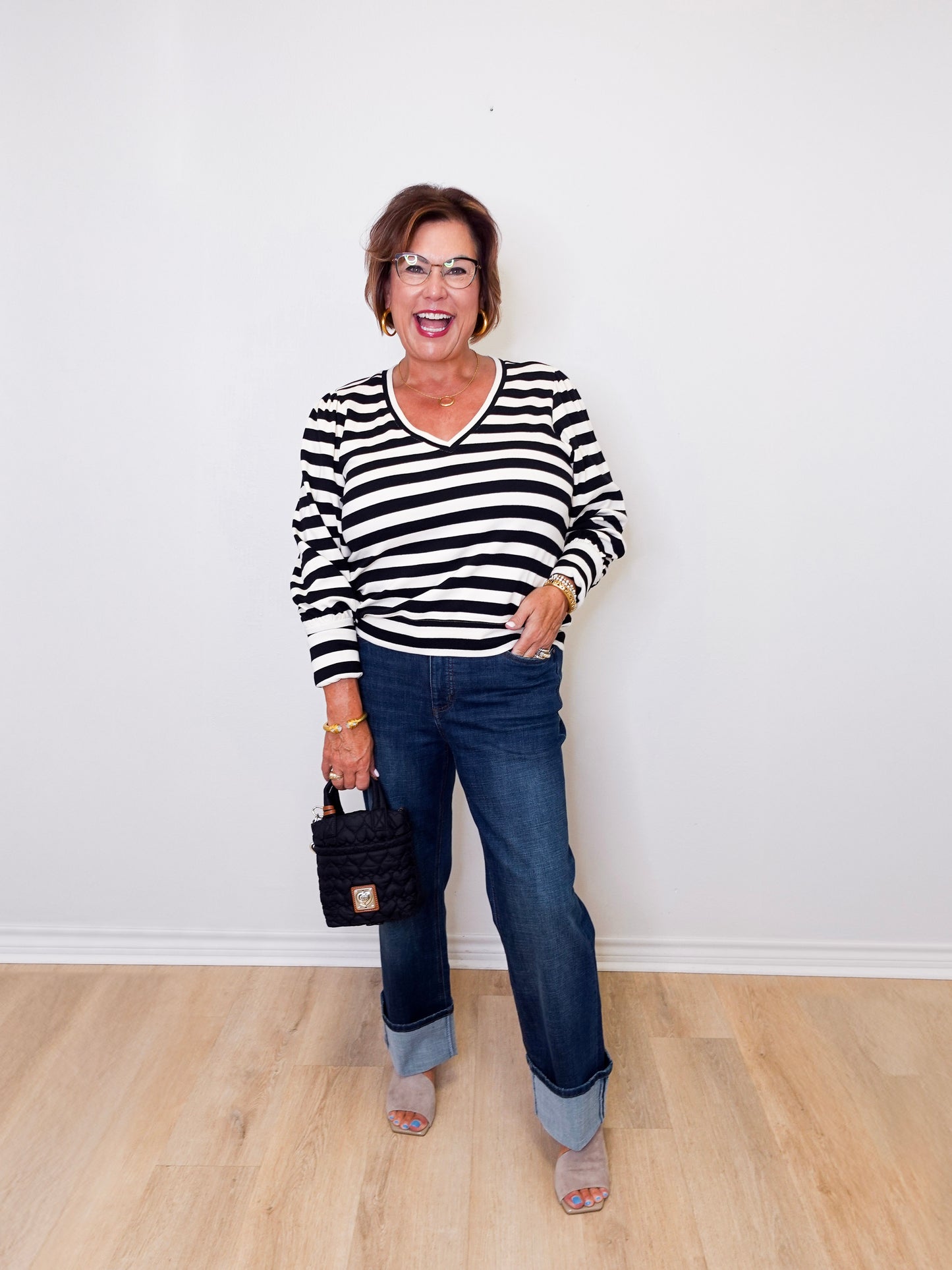Woman wearing a black and white striped sweater and blue jeans, standing against a white wall.