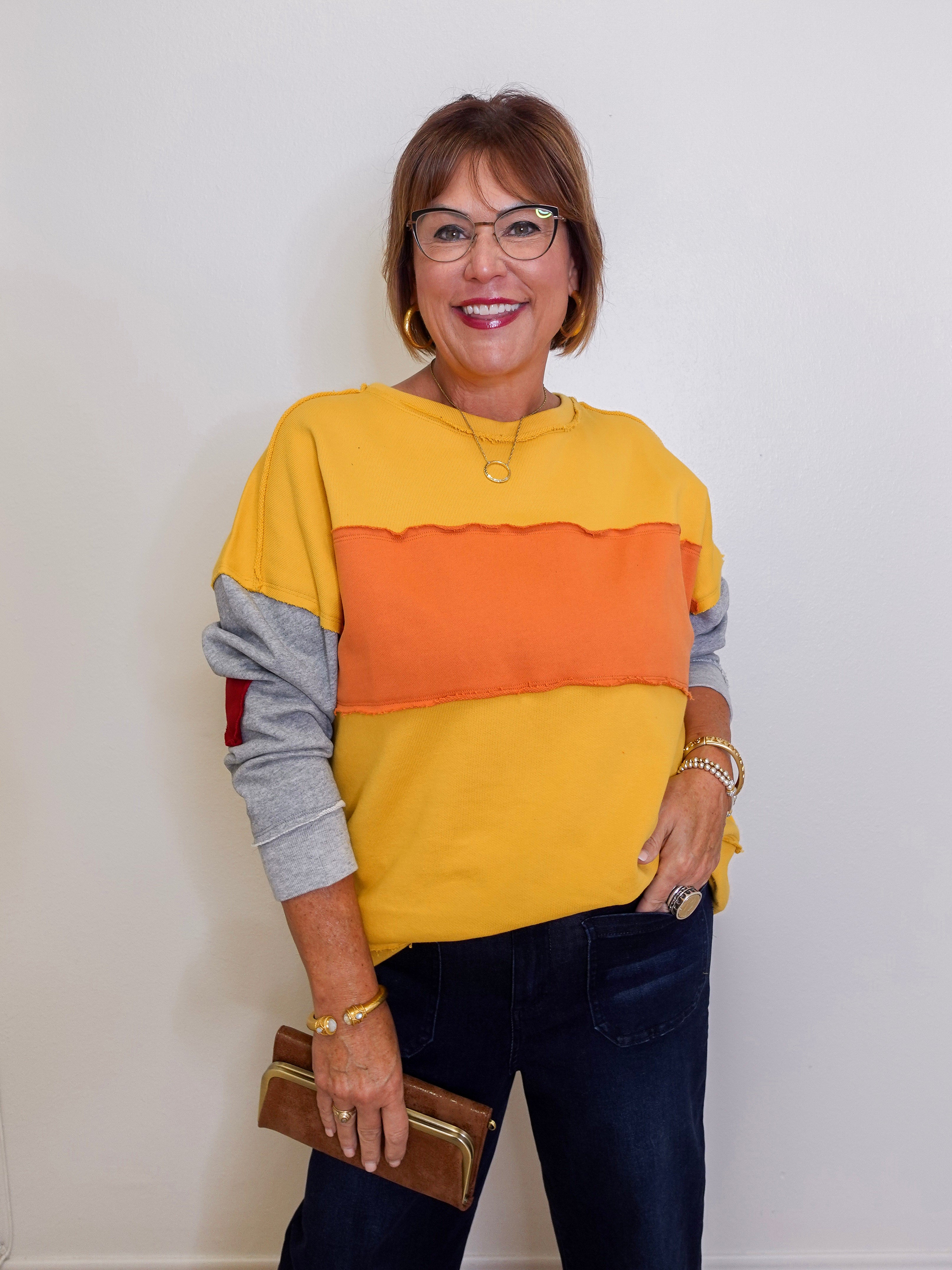 Woman wearing a yellow, orange, and gray sweater with dark jeans against a white background