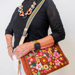 Woman holding a brown handbag with floral embroidery against a white background