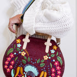 Handbag with floral and rooster design held by a person wearing a white sweater.