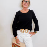 Woman wearing a black top and white pants with a floral clutch against a white background