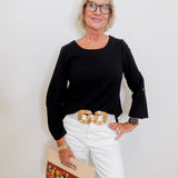Woman wearing a black top and white pants with a floral clutch against a white background