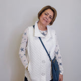 Woman wearing a white quilted vest over a star-patterned shirt with a blue crossbody bag against a plain background.