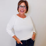 Woman wearing a white top and dark jeans against a plain background