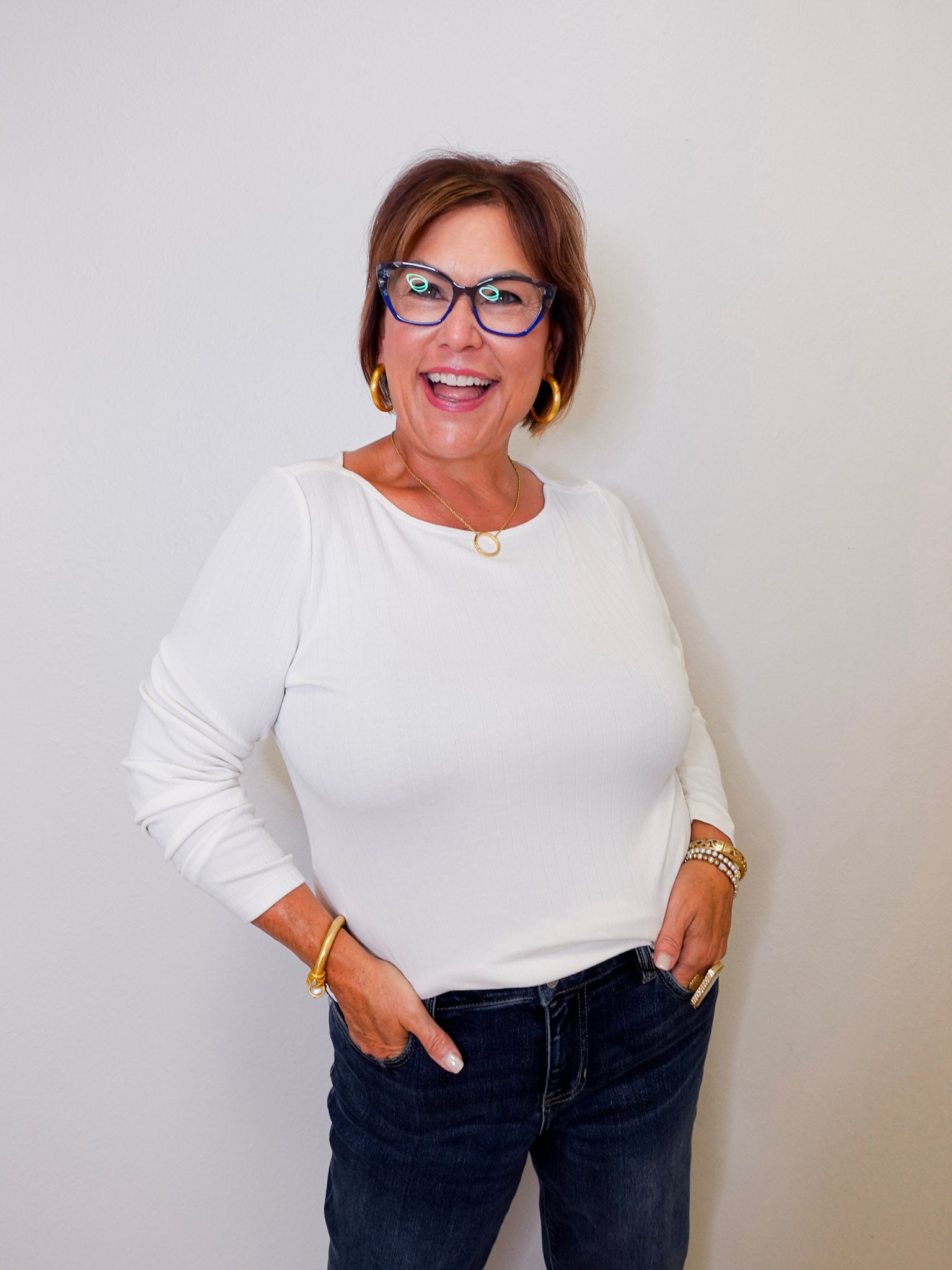 Woman wearing a white top and dark jeans against a plain background