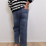 Person wearing a black and white striped sweater and blue jeans against a white wall.