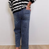 Person wearing a black and white striped sweater and blue jeans against a white wall.