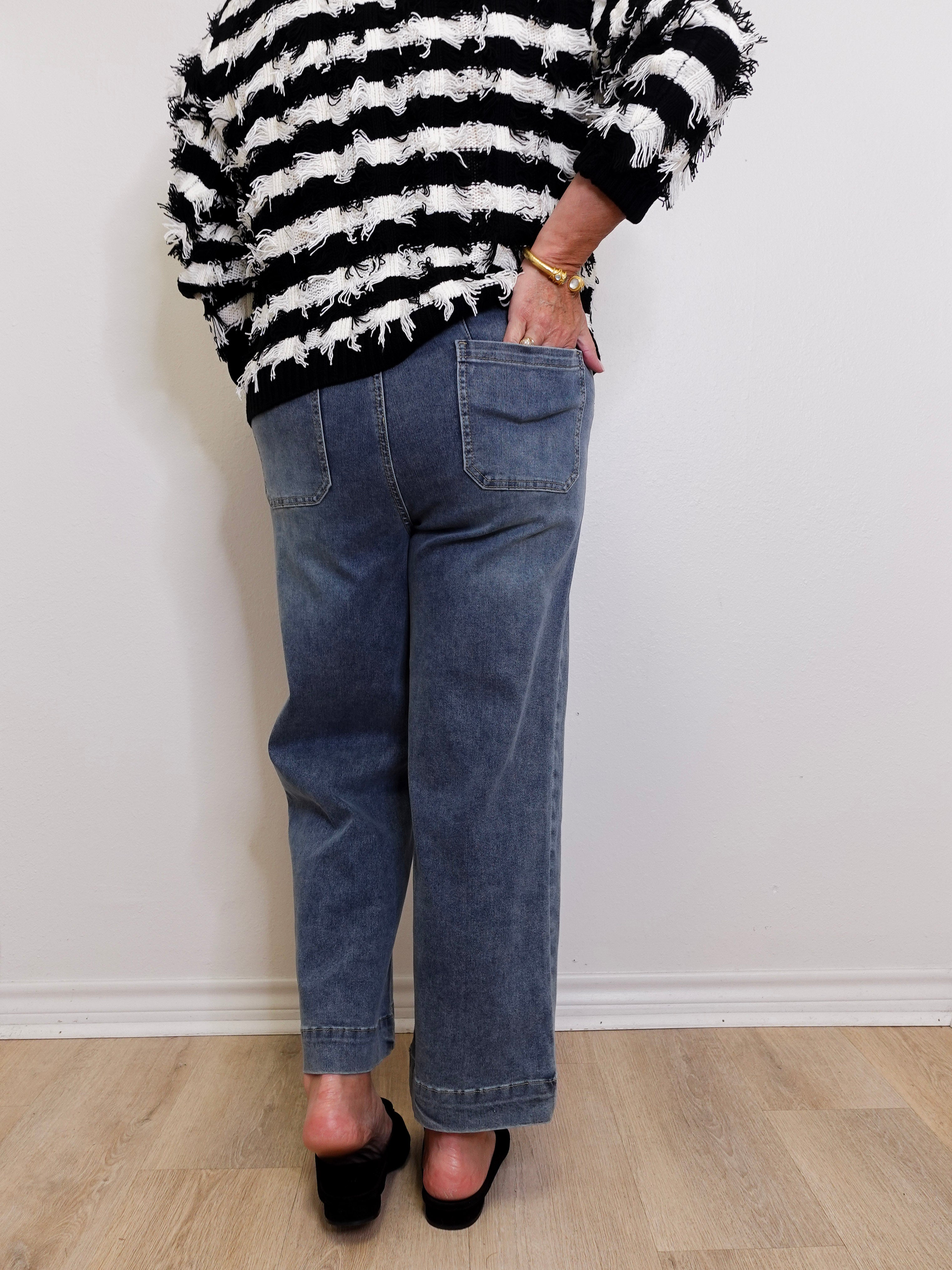 Person wearing a black and white striped sweater and blue jeans against a white wall.