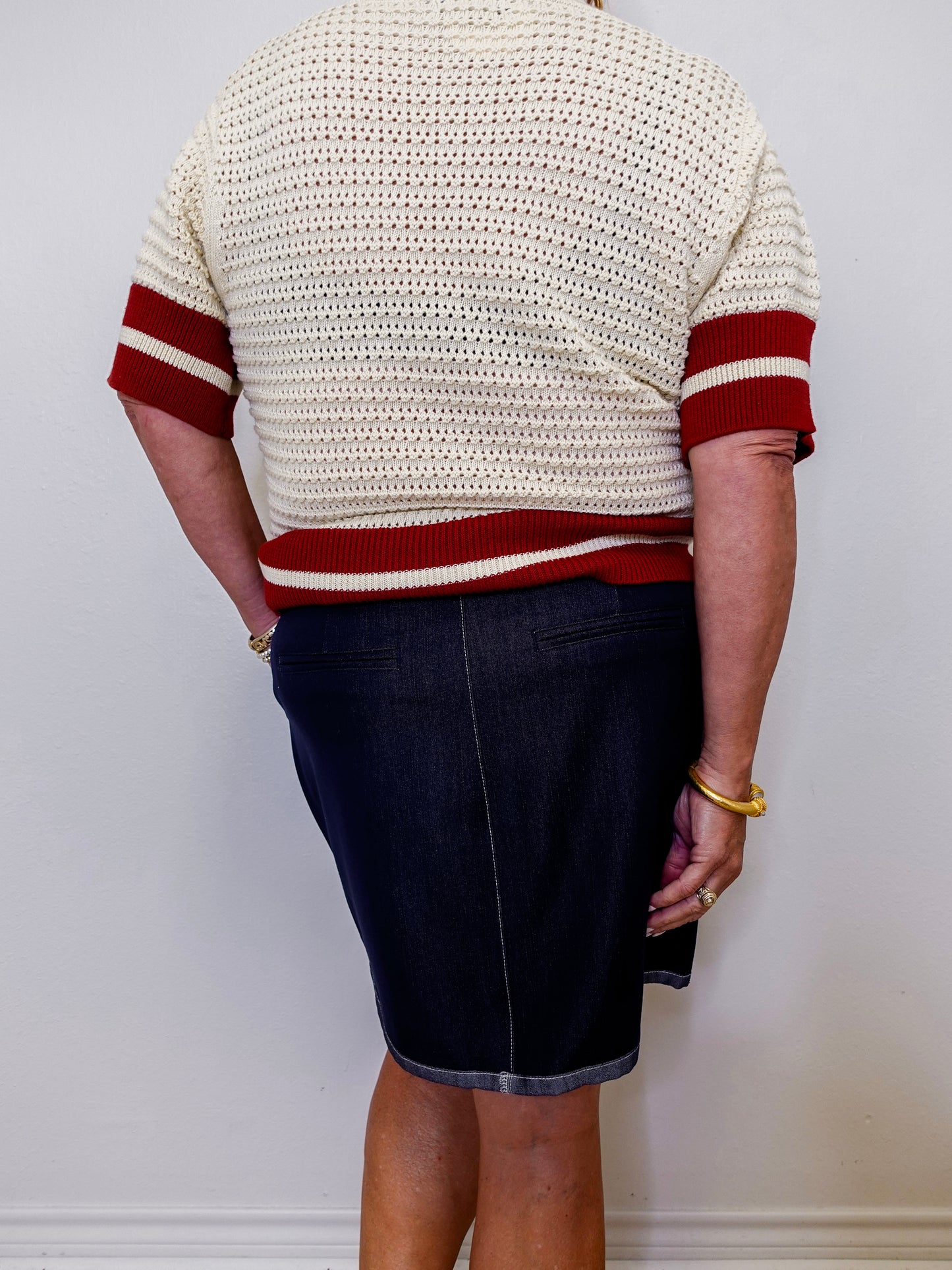 Person wearing a cream sweater with red stripes and a dark denim skirt against a white background