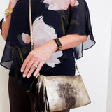 Woman holding a gold clutch purse with a floral top and black pants.
