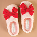 Pair of fluffy slippers with red bows on a beige background
