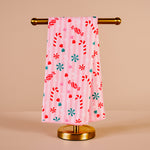 Pink towel with candy cane and snowflake pattern on a gold towel rack against a beige background