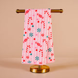 Pink towel with candy cane and snowflake pattern on a gold towel rack against a beige background