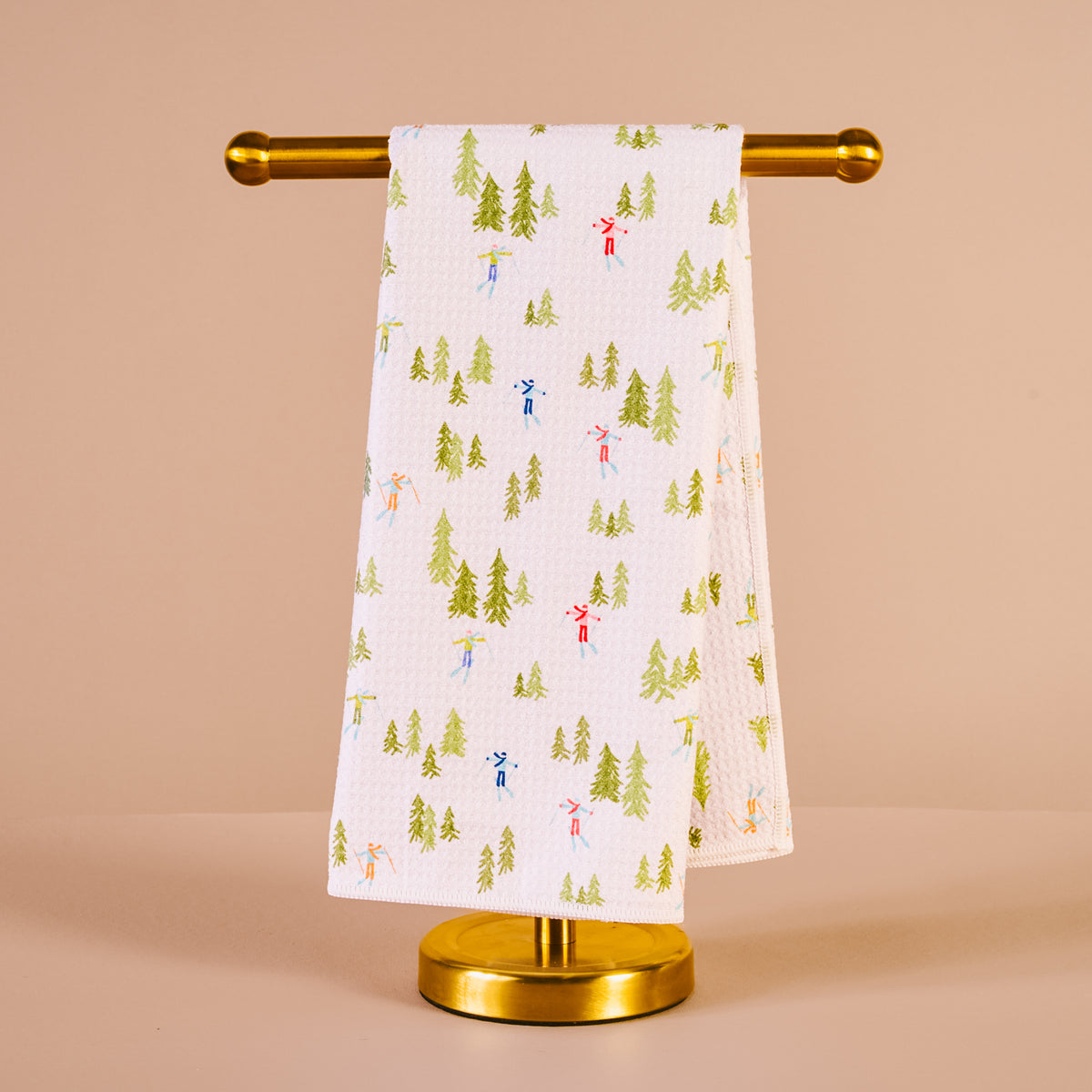 Towel with a Christmas tree and reindeer pattern on a gold towel rack against a beige background
