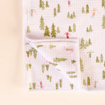 Baby blanket with forest and skier pattern on a light pink background
