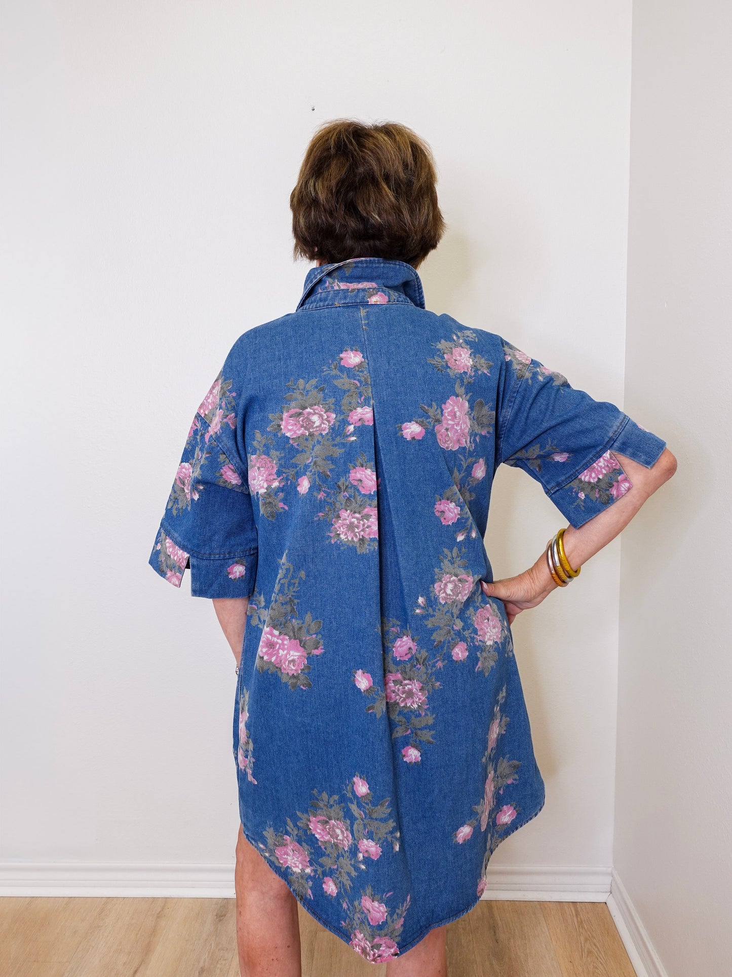 Person wearing a blue floral dress against a white wall