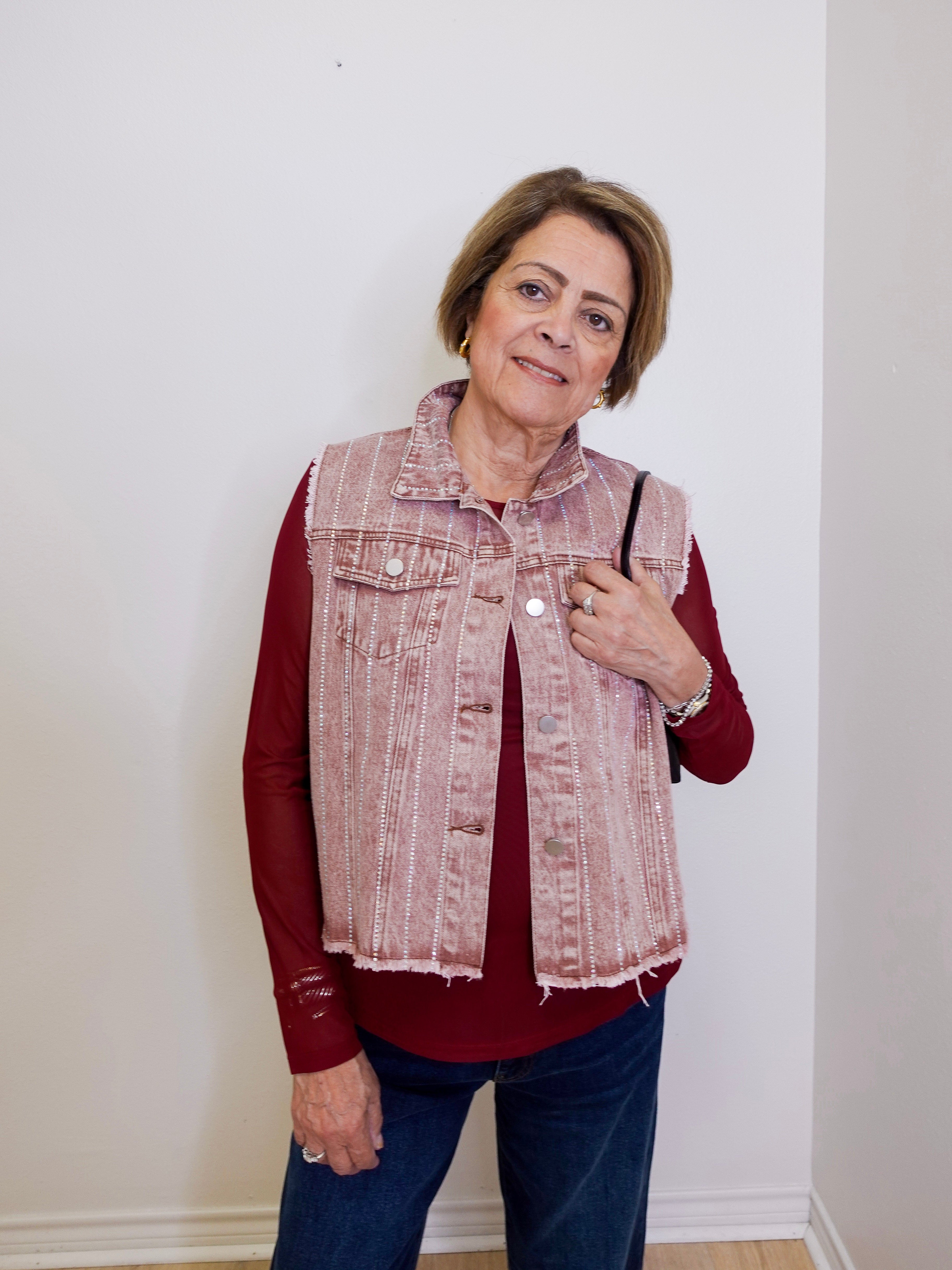 Woman wearing a red shirt and denim vest against a white wall