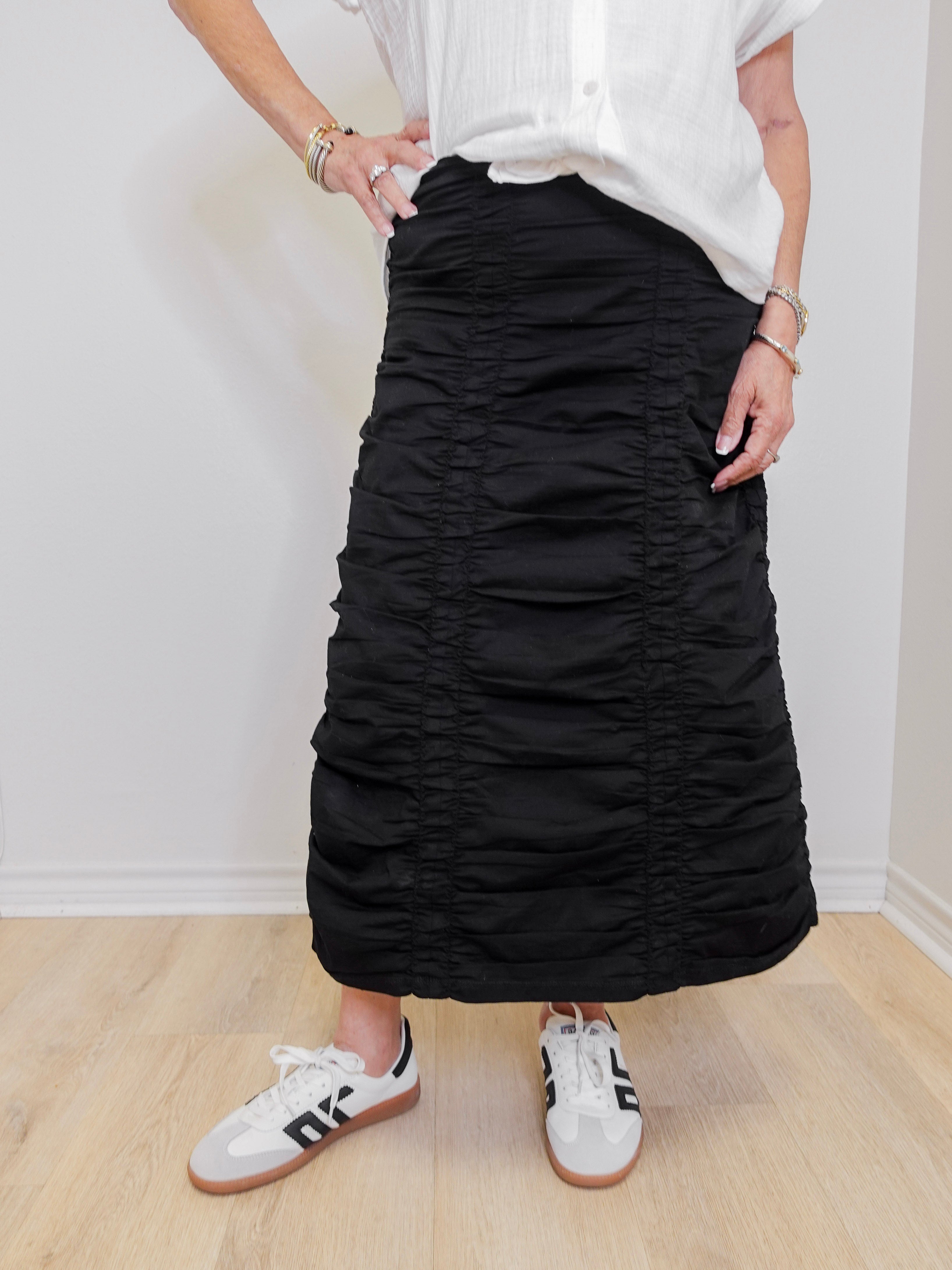 Person wearing a black ruched skirt and white sneakers on a plain background