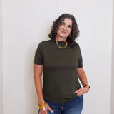 Woman wearing an olive green t-shirt and blue jeans against a white wall