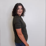 Woman wearing a green t-shirt and blue jeans against a white wall