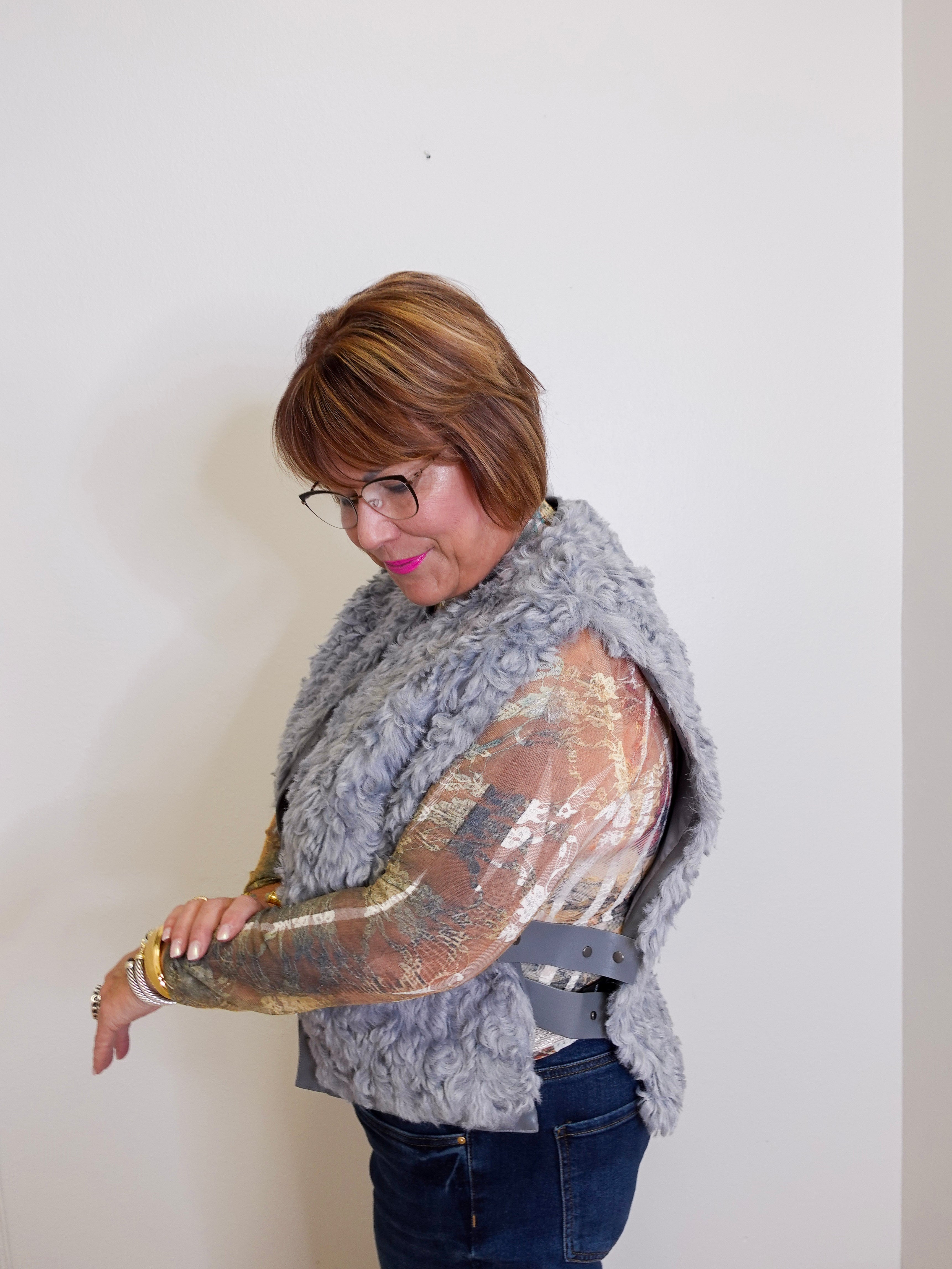 Woman wearing a gray fur vest over a gold sequin top against a white background