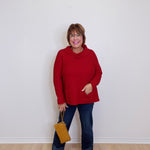 Woman wearing a red sweater and blue jeans, holding a yellow bag against a white background