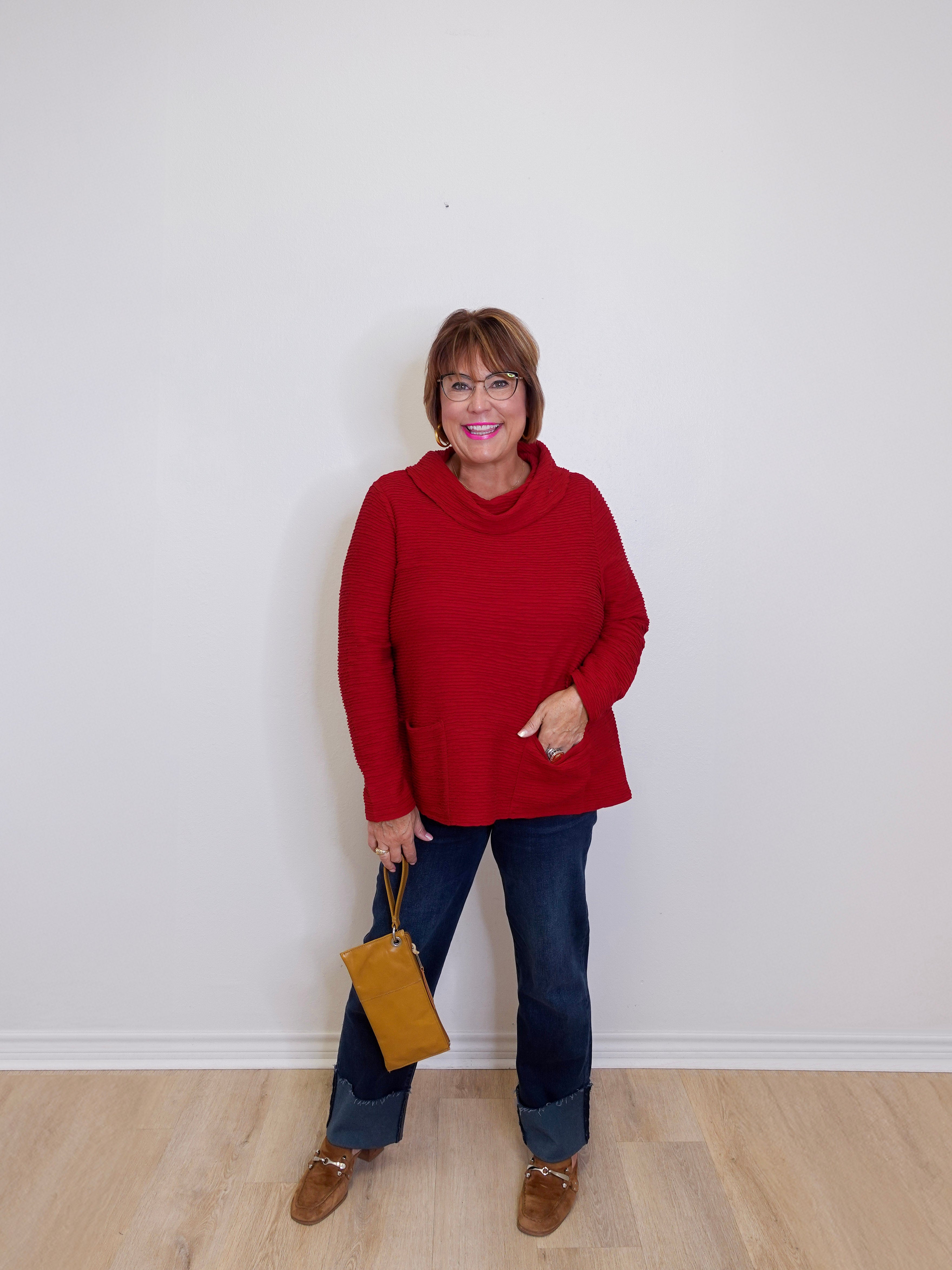 Woman wearing a red sweater and blue jeans, holding a yellow bag against a white background