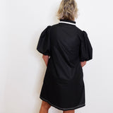 Person wearing a black dress with puffed sleeves against a white wall