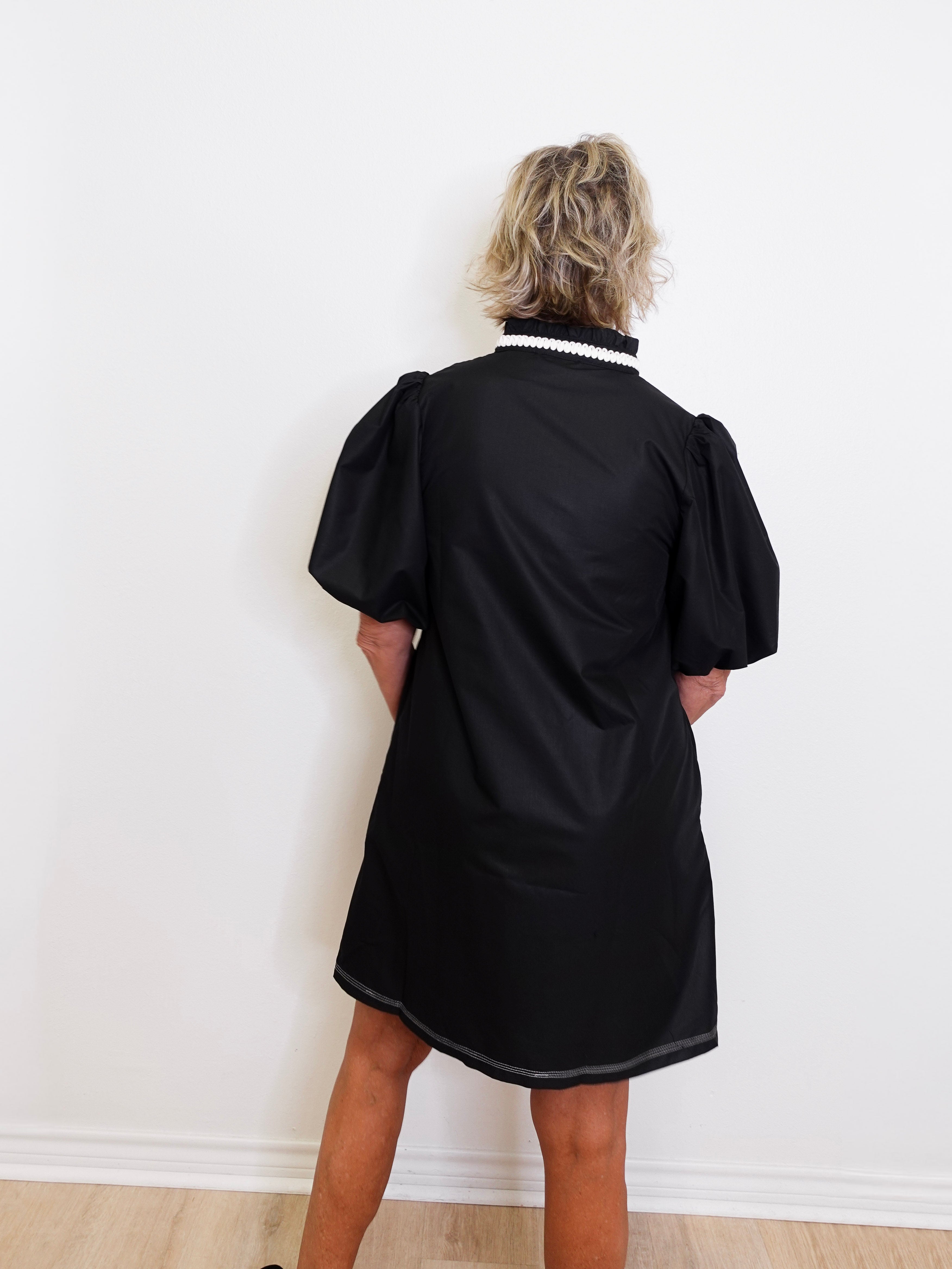Person wearing a black dress with puffed sleeves against a white wall
