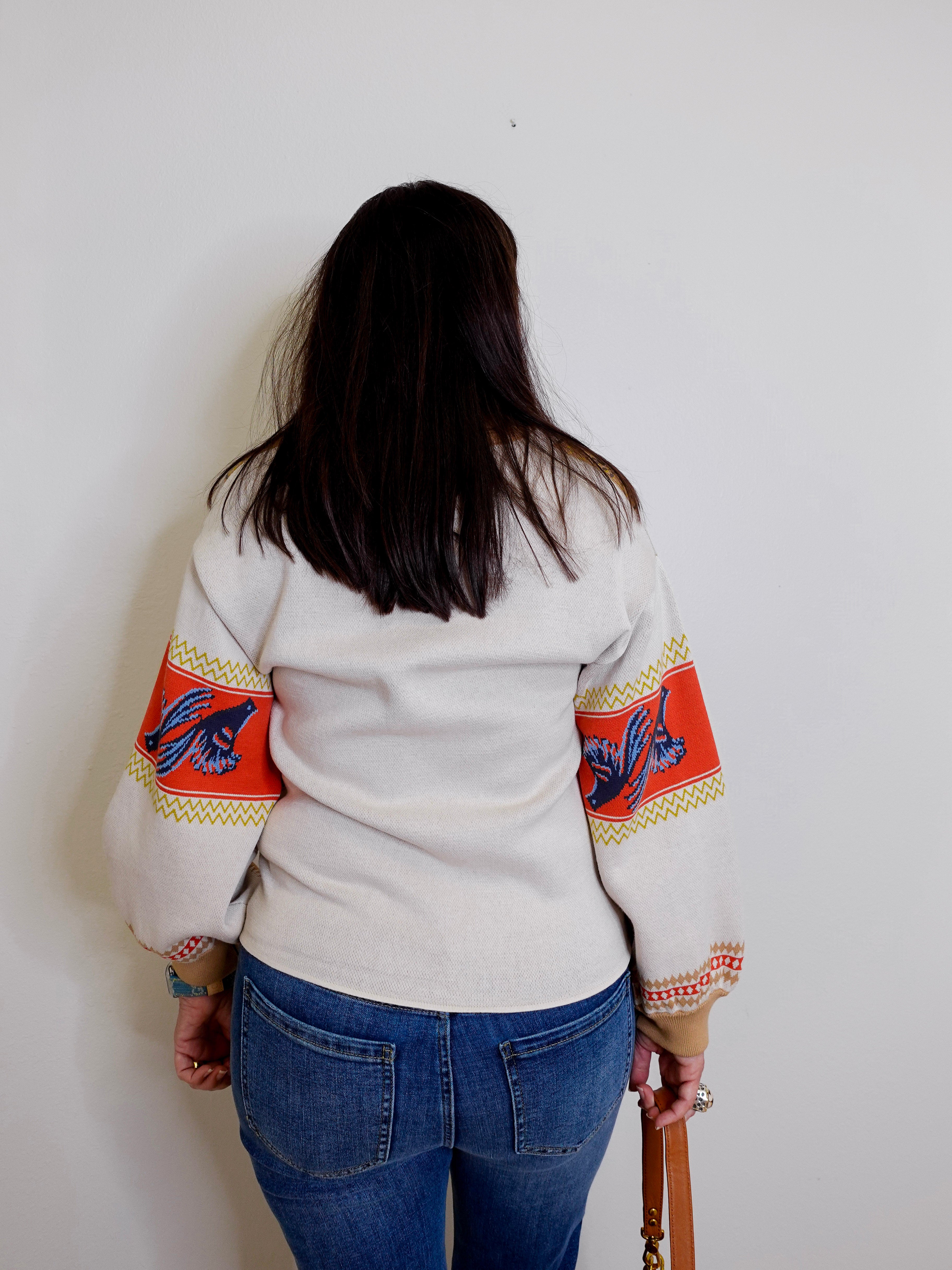 Person wearing a white sweater with colorful arm designs against a plain background