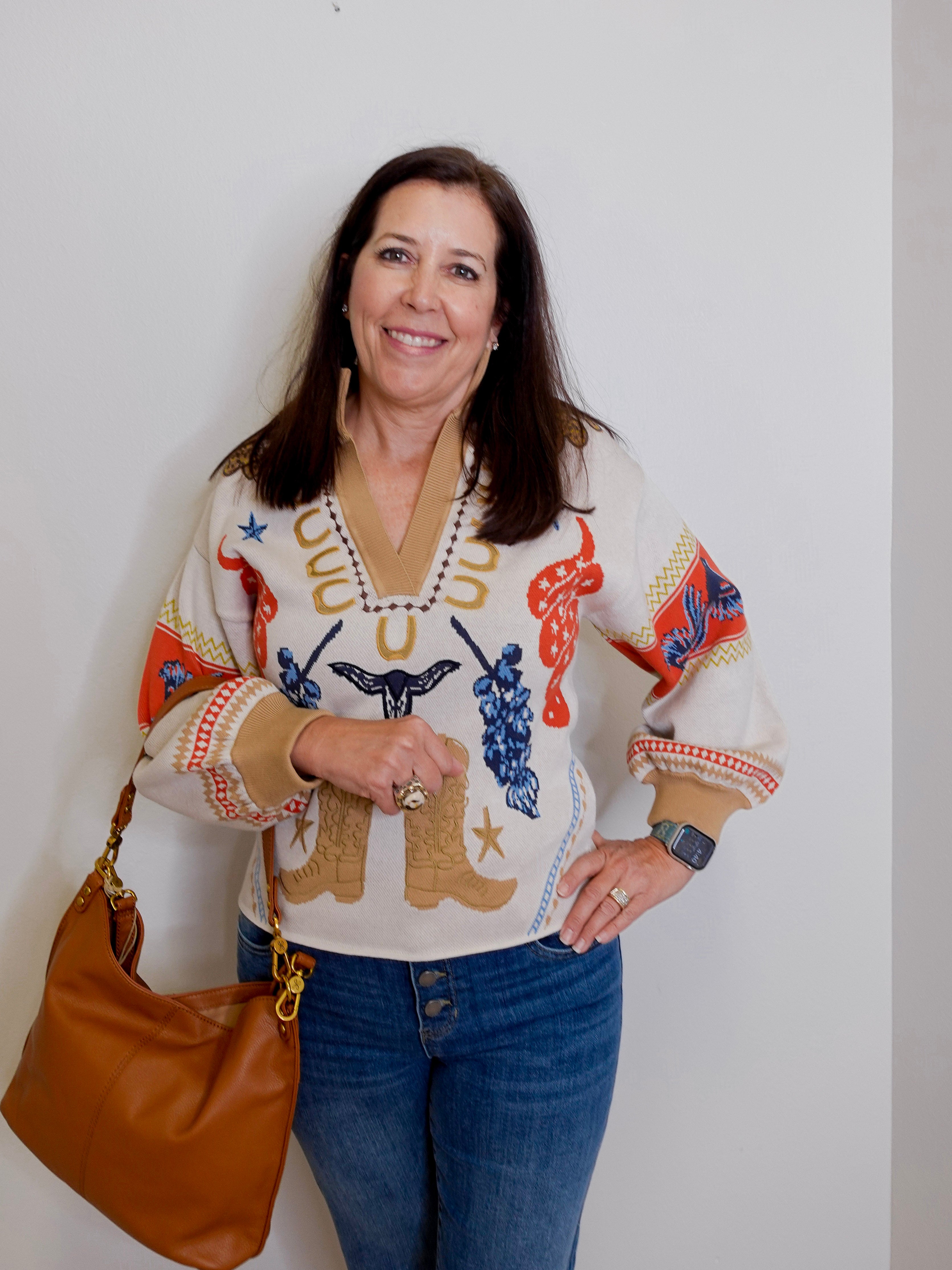 Woman wearing a colorful sweater with animal prints, holding a brown bag against a plain background