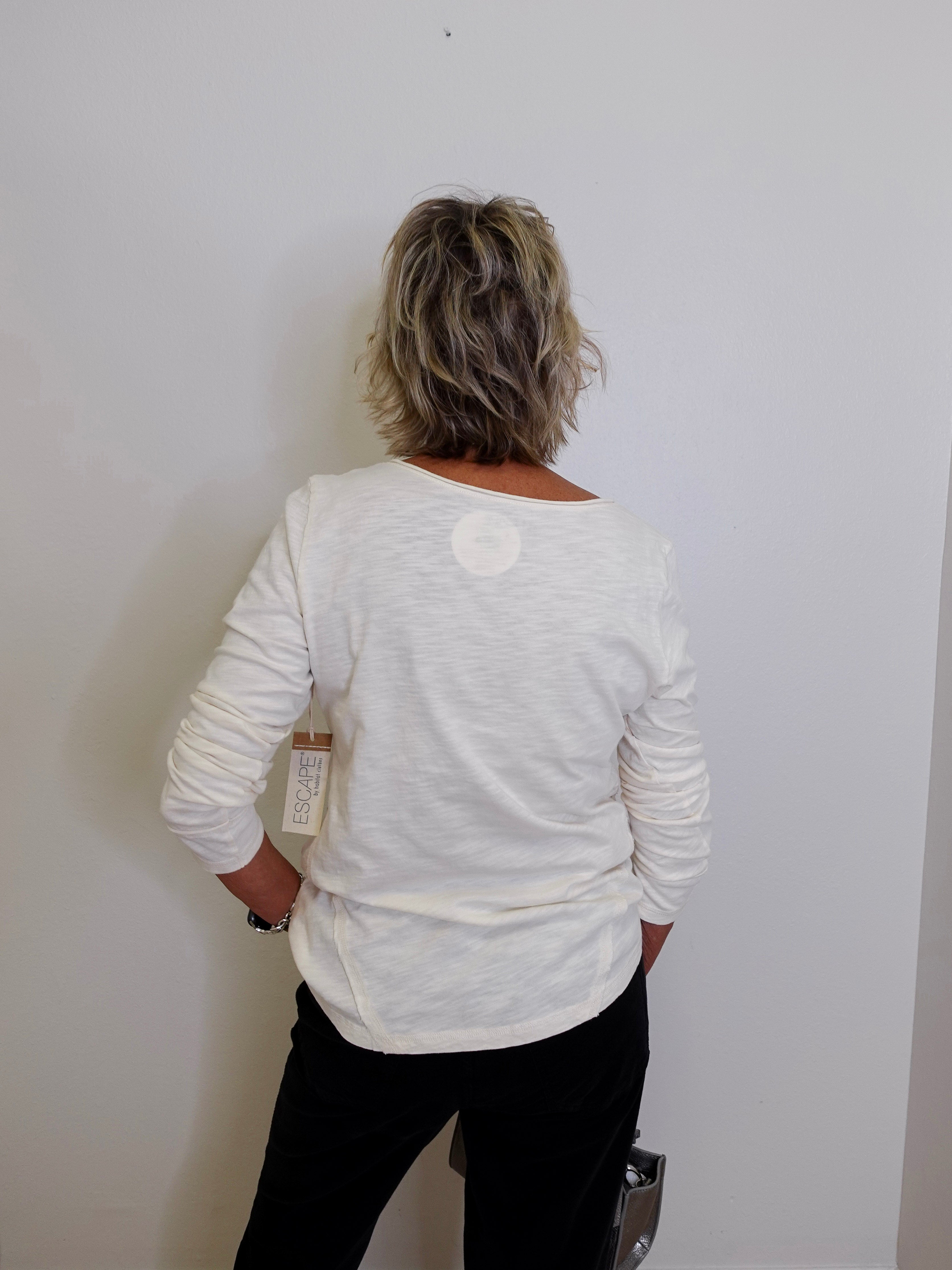 Person wearing a white long-sleeve shirt against a plain white wall
