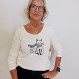 Woman wearing a white sweater with a cat design against a plain background