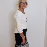 Woman in a white sweater holding a gray handbag against a plain wall.