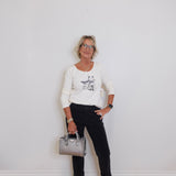 Woman standing against a white wall holding a silver handbag.