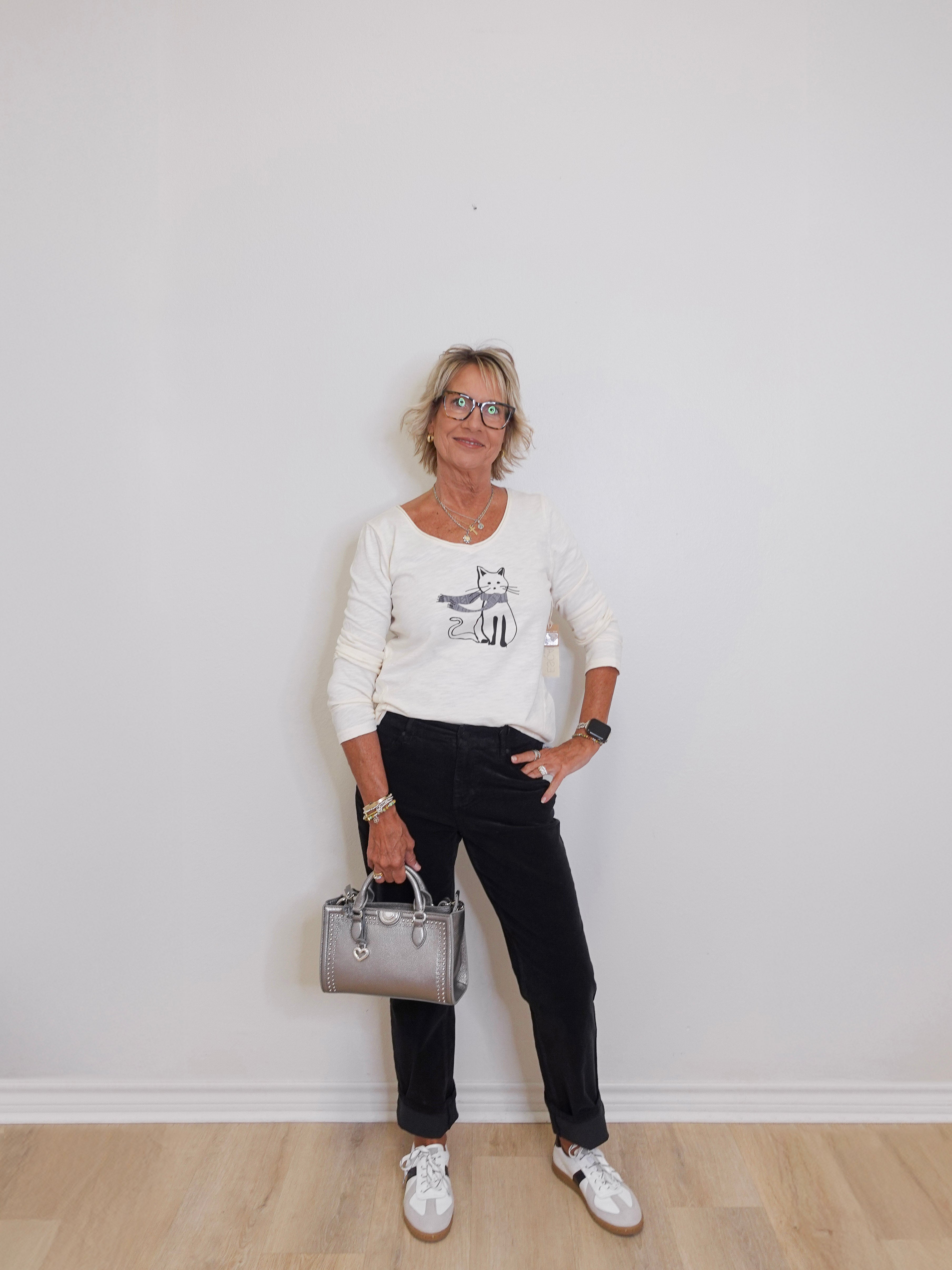Woman standing against a white wall holding a silver handbag.