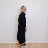 Person wearing a black dress standing against a white wall.